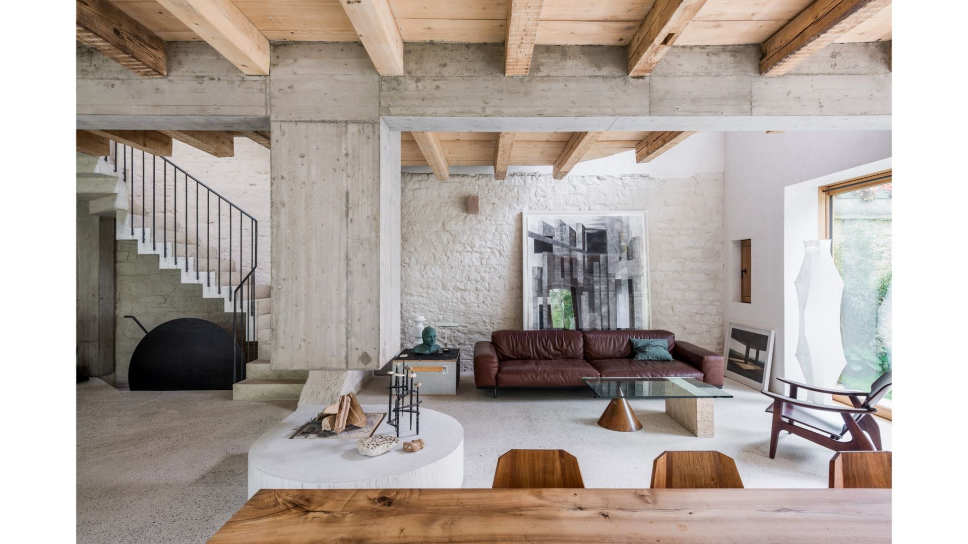 Im Gartengeschoss gehen die Bereiche Wohnen und Essen offen ineinander über. Die Holzbalkendecke wurde freigelegt und ein Querträger aus Beton samt skulpturalem Cheminée ergänzt. (Hinter dem Sofa: Gemälde «Untitled 2010» von Thomas Hauri)