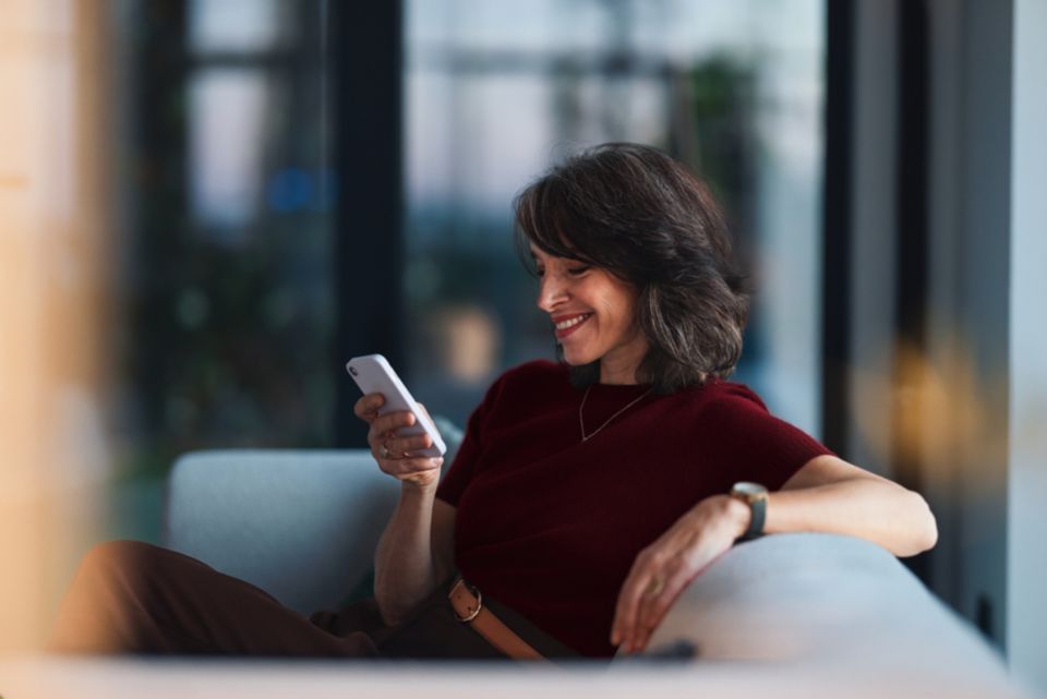 Una donna è seduta su un divano, guarda il cellulare e ride.
