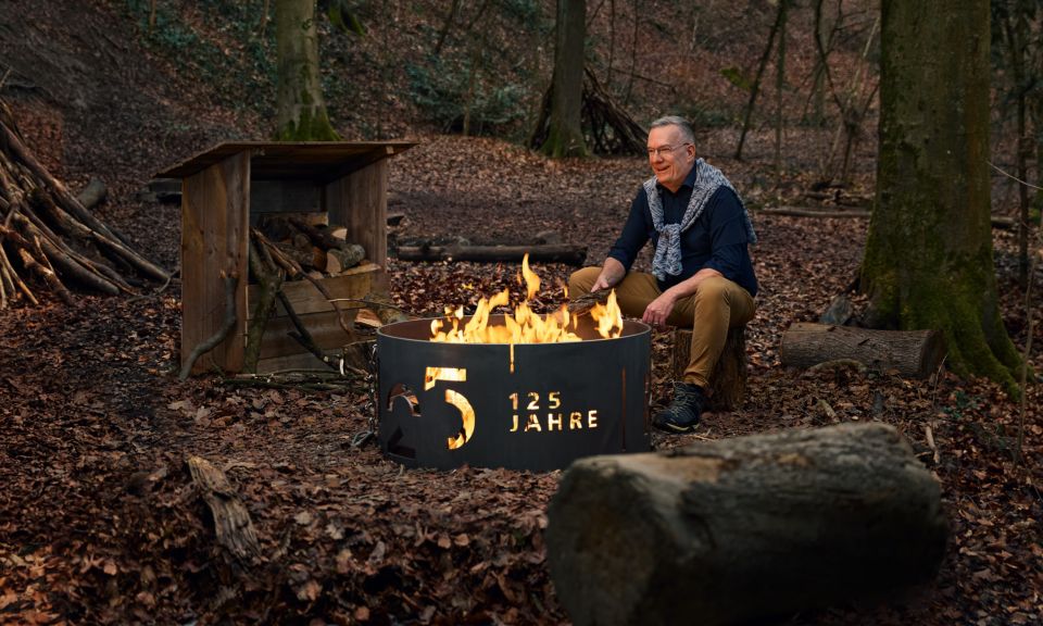 Mann sitzend an einer Feuerstelle im Wald