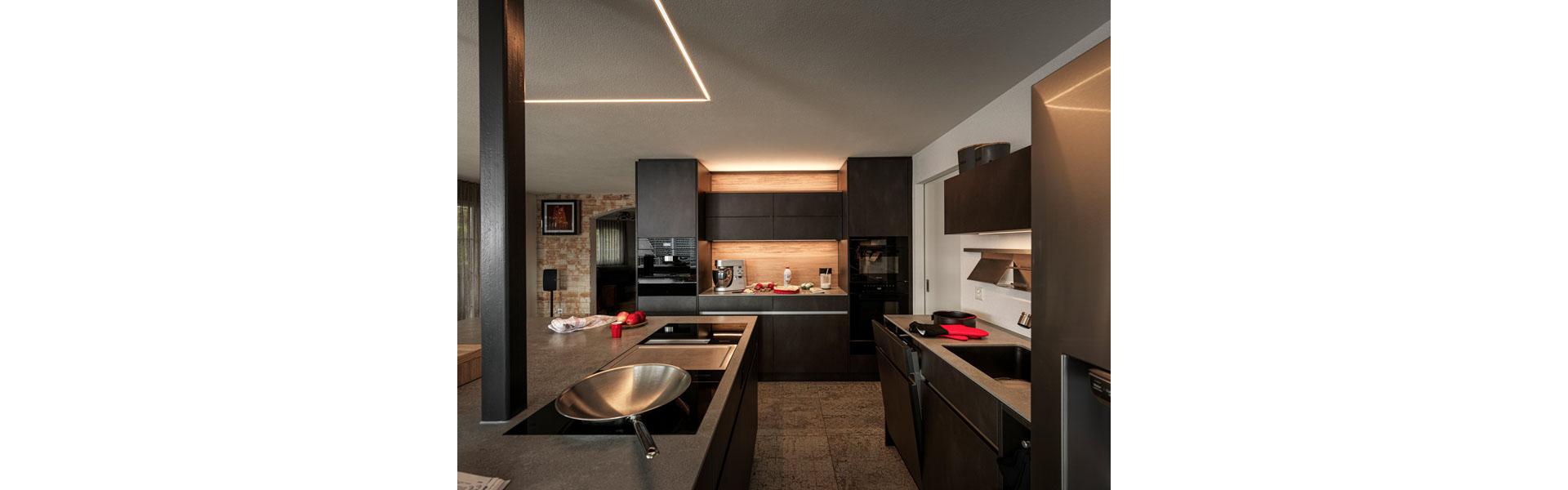Grazie al suo concetto di illuminazione, questa cucina di Veriset è letteralmente il punto luce della casa. La luce diretta e indiretta immerge questa cucina dall'aspetto industriale, con frontali in acciaio grezzo, rovere e rivestimenti in ceramica grezza, in un'atmosfera suggestiva. Foto: Veriset