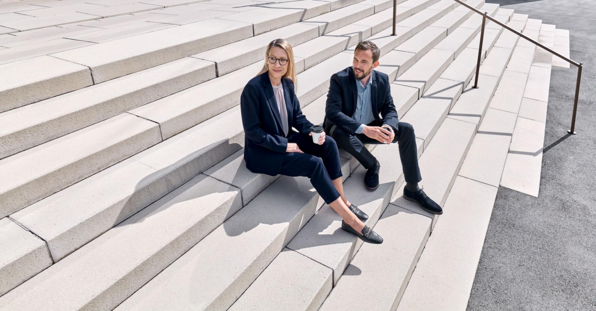 Zwei Raiffeisen Mitarbeitende sitzen auf einer Treppe.