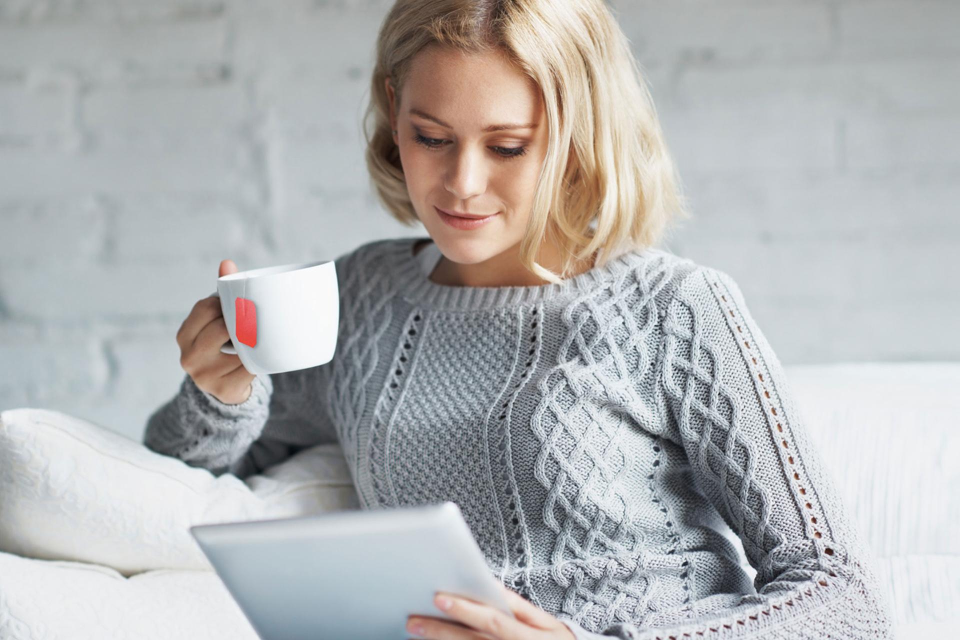 Frau mit Teetasse schaut in Tablet