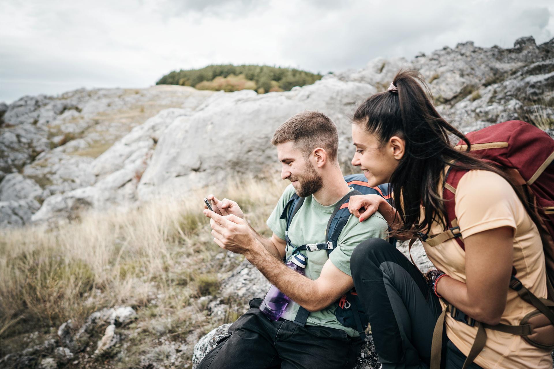 Wanderer sitzen auf Fels und schauen auf Mobile