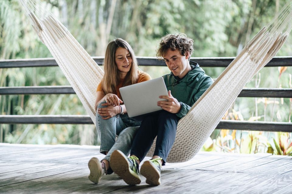 Mann und Frau schauen auf einen Laptop in der Hängematte