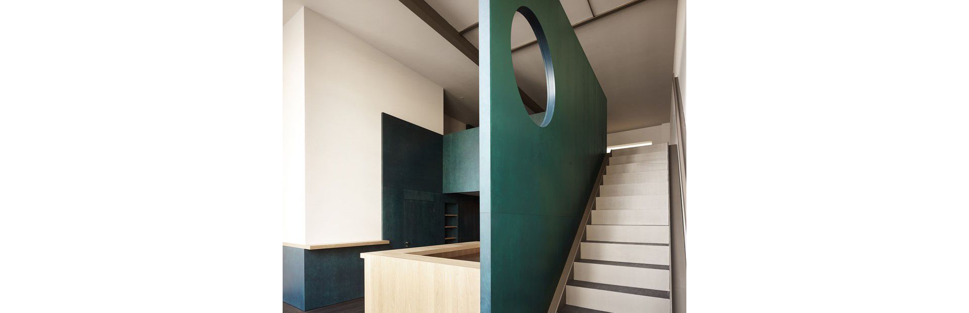 Derrière la paroi en bois, un escalier mène à un deuxième niveau d’utilisation. Le trou poinçonné dans la cloison confère à la construction une légèreté ludique.