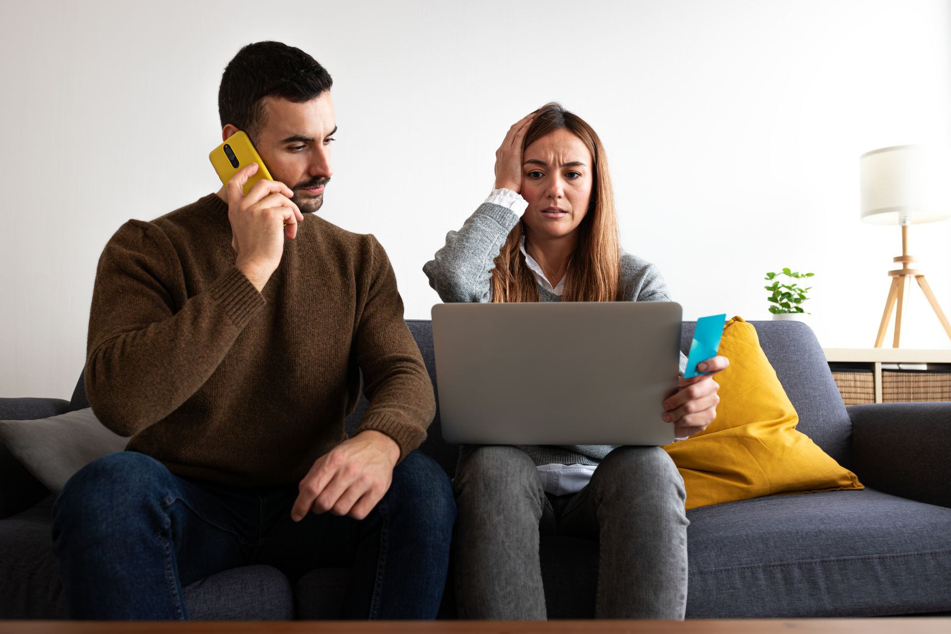 Young couple having financial problems calling bank. Female holding credit card with worried expression.