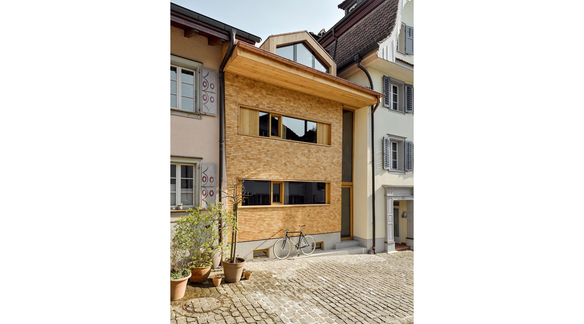 La façade nord est habillée d’une fine texture de bardeaux en mélèze. Grâce au vitrage élancé sur deux étages, la ruelle, qui passait autrefois devant la maison, est de nouveau perceptible.