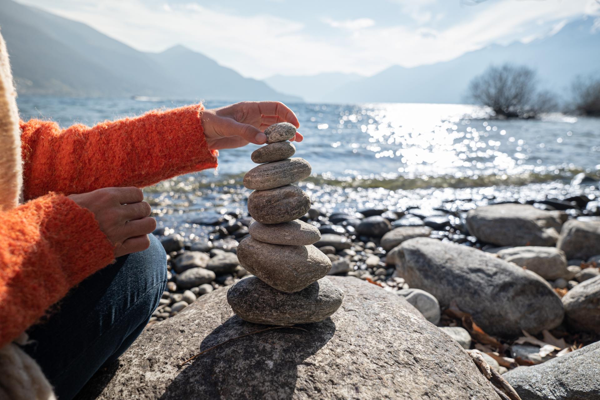 Hand stapelt Steine zu einem Turm am Wasser