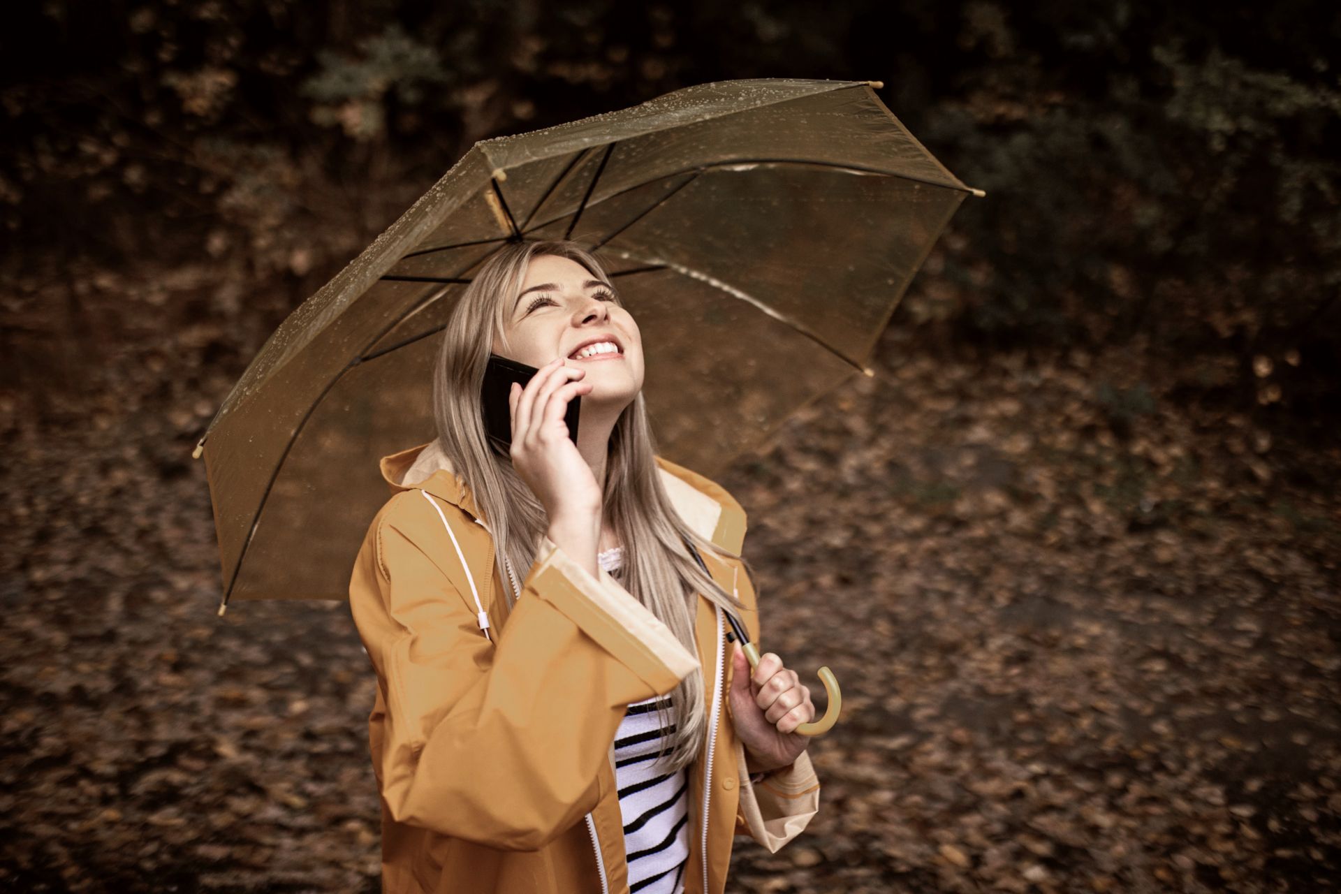 Giovane donna con impermeabile giallo che usa lo smartphone in una giornata di pioggia.