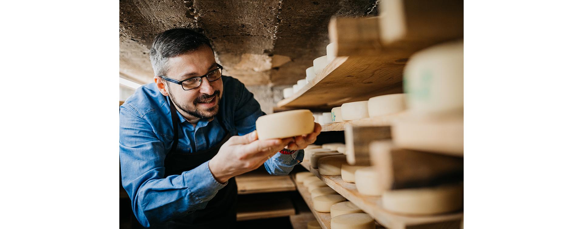 Handsome cheesemaker is checking cheeses in his workshop storage