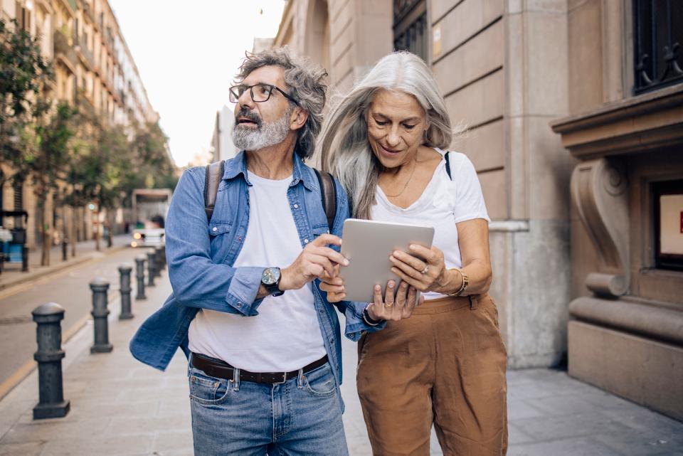 Älteres Touristenpaar, Frau und Mann, laufen durch eine Stadt und halten ein Tablet in der Hand.