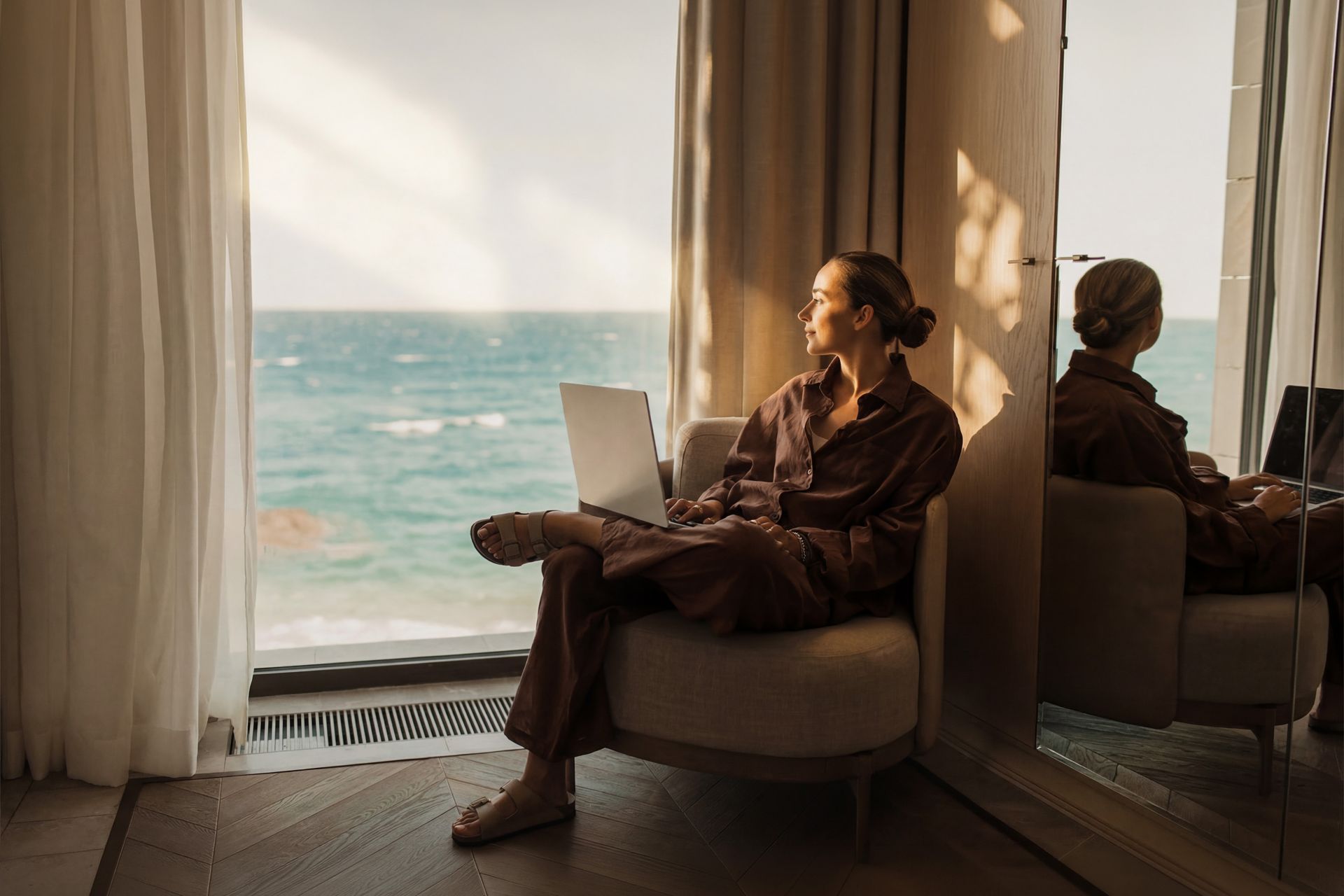 Frau sitzt mit dem Laptop vor dem Fenster und schaut nach draussen