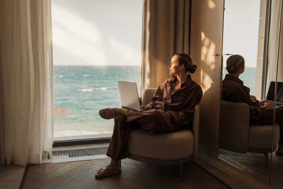 Frau sitzt mit dem Laptop vor dem Fenster und schaut nach draussen