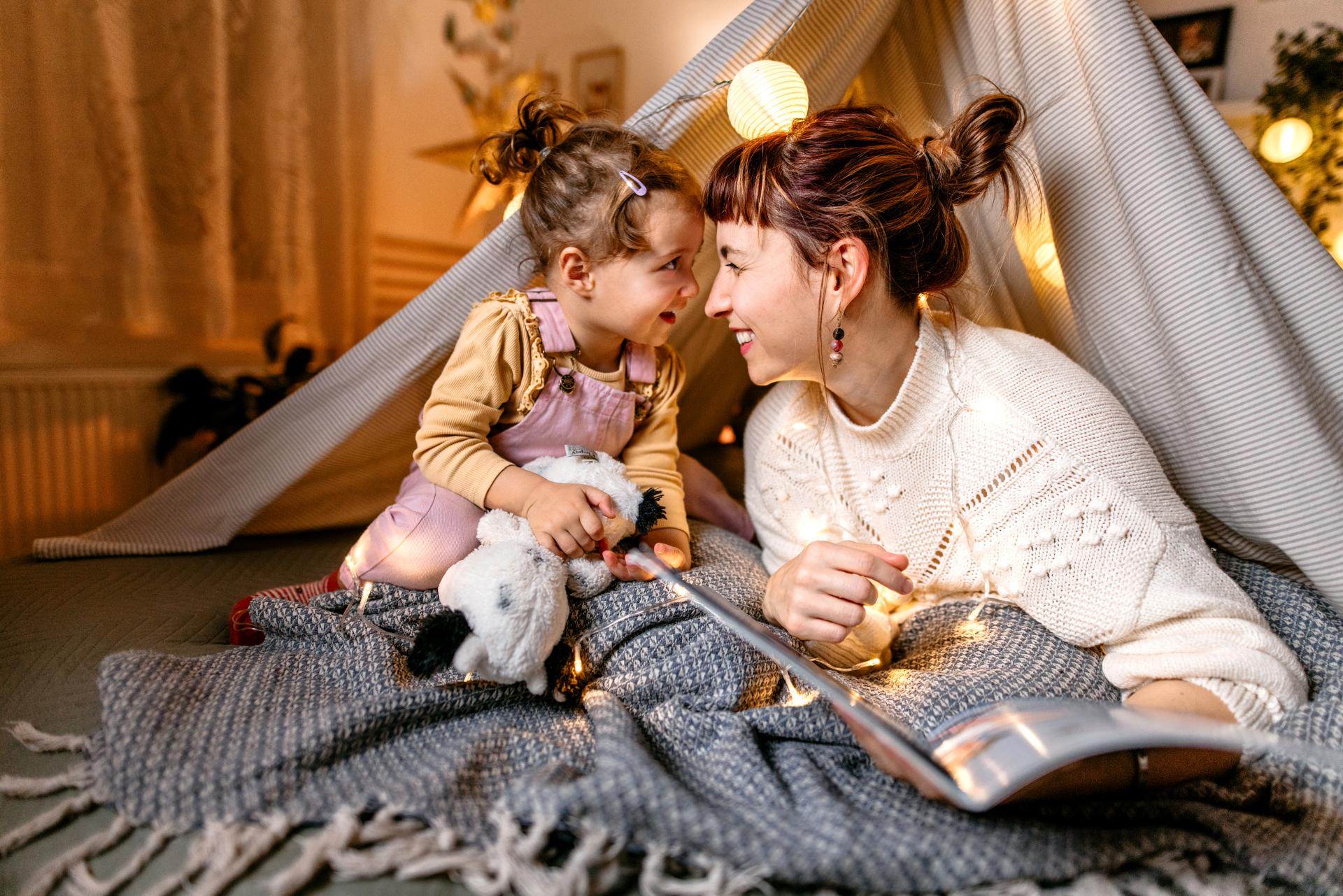 Mutter und kleine Tochter lesen gemeinsam ein Buch im Wohnzimmer in einem kleinen Zelt.